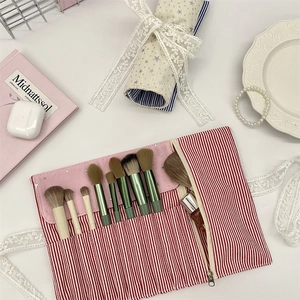 Pink star makeup brush set with 9 green handles in a red striped roll-up pouch