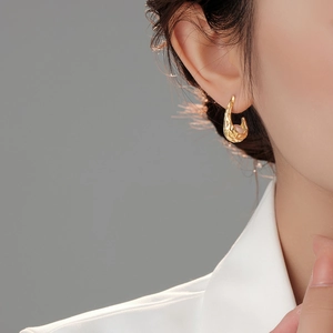 Dettaglio degli orecchini dorati con texture irregolare indossati con perla minimale