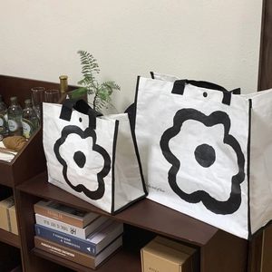 Detail of white woven tote bag set with black floral patterns and text on wooden shelf
