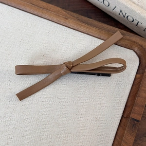 Close-up of brown PU leather bow hair clip showing detailed texture on wooden tray