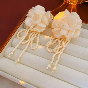 Detail of fabric flower earrings with beaded tassels in a white jewelry display box