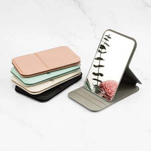 Portable folding makeup mirror in colorful faux leather covers on marble surface