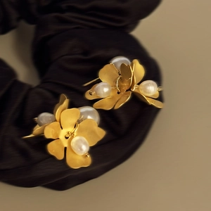Close-up of golden flower stud earrings with white pearls on dark silk fabric