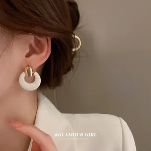 Close-up of white hoop earrings with gold rectangle links worn on a model in white