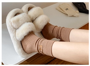 Detail of beige plush slippers paired with beige cotton socks featuring a bow embroidery