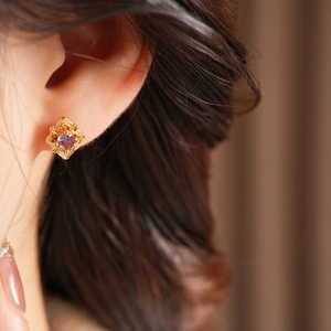 Close-up of vintage gold rhombic earrings with purple zircon inlay worn by a model