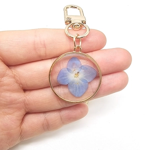 Golden keychain with real blue dried flowers in a round frame on white background