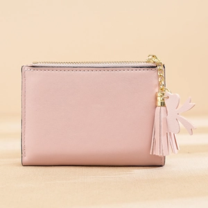 Pink leather wallet detail with gold zipper, tassel pendant and decorative bow charm
