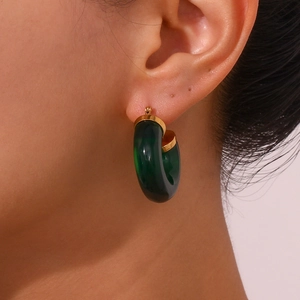 Detail of chunky C-shape hoop earrings with green acrylic resin and gold metal plating
