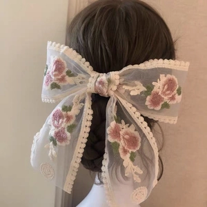 Detailed back view of a beige lace hair bow with pink floral embroidery on braided hair