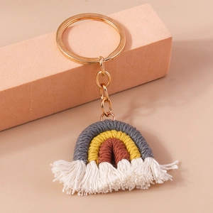 Detailed shot of handmade woven rainbow keychain with white tassels on warm orange backdrop