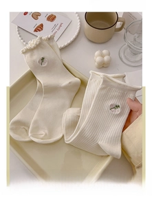 Close-up of cream-colored crew socks with floral embroidery and lace trim on a tray