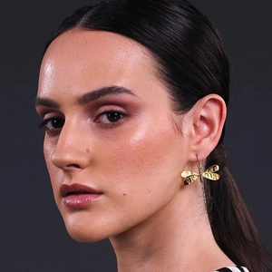 Golden dragonfly drop earrings with hammered metal texture on a female model