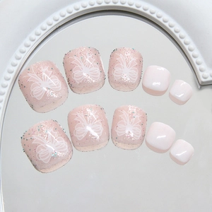 Pale pink shimmering press-on toenails with white bow designs on a round mirror