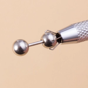 Macro shot of a four-prong stainless steel pick-up tool holding a small silver bead