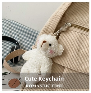 Detalle de un colgante de oso de peluche blanco en una mochila de pana beige