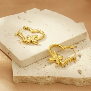 Macro detail of golden heart-shaped earrings with flower relief on textured stone