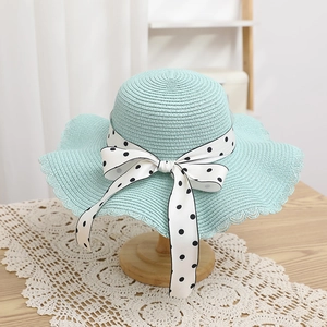 Close-up of mint green straw hat with polka dot bow and woven wavy brim details