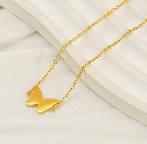 Detail of a polished gold butterfly charm on a fine chain over silk fabric