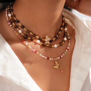 Detail of layered gold-plated necklace with tiger eye stones and zircon butterfly pendant