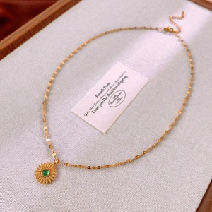 Close-up of golden sunflower pendant necklace with green gemstone on fabric background