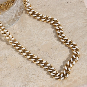 Detailed close-up of golden Cuban link necklace with white enamel inlays on stone surface