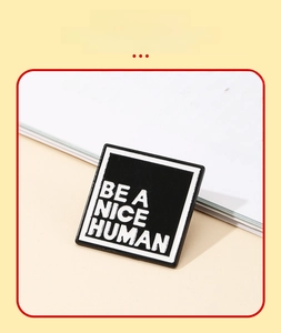 Close-up of square metal enamel pin with BE A NICE HUMAN slogan on beige book background