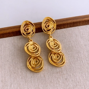 Detailed macro shot of three-tier golden spiral drop earrings on a linen background