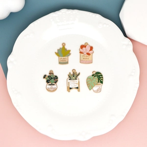 Detail of five enamel succulent plant charms with gold metal edges on a decorative plate