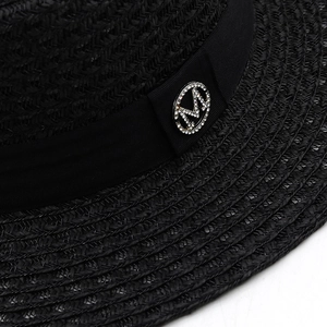 Close-up of black woven straw hat featuring a rhinestone letter M on a grosgrain ribbon