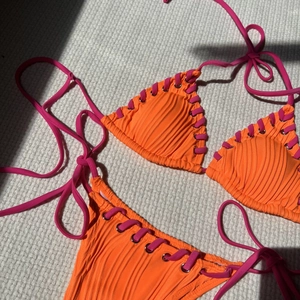 Detail of orange ribbed bikini fabric with pink lace-up ties and silver eyelet hardware