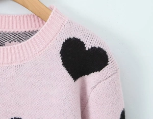 Detail of pink knitted sweater showing soft fabric texture and black heart patterns