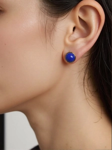Macro view of a gold-framed round dark blue lapis lazuli stud earring worn by a model