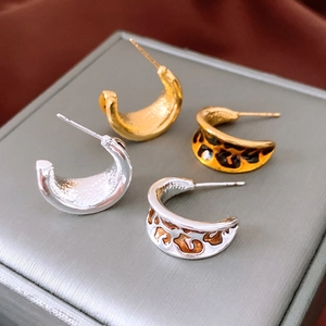 Close-up of vintage C-shape hoop earrings in gold, silver, and leopard resin finish