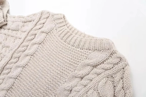 Macro detail of beige cable knit sweater showing ribbed crew neck and textured stitching