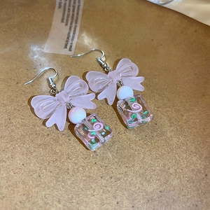 Detail of pink bow and square resin pendant earrings with silver hook on cork texture