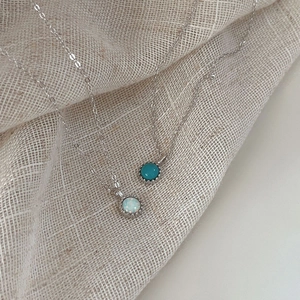 Macro detail of S925 sterling silver opal and turquoise round necklaces on linen fabric
