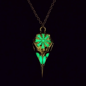 Close-up of golden bird skull pendant with glowing green rune patterns on black background