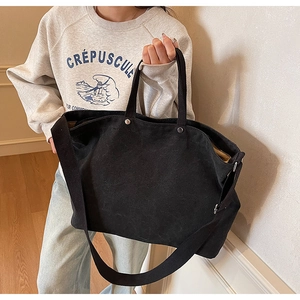 Black canvas tote bag shown as a crossbody and handbag on a model in a cozy indoor setting