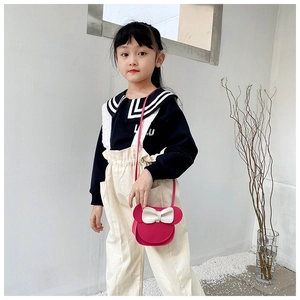 Pink girls crossbody bag with white bow and cartoon ears worn by a child model