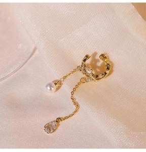 Detail of gold-plated ear clip with pearl and teardrop gemstone on gold silk fabric