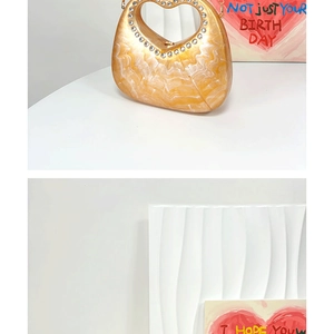 Detail of gold marble acrylic handbag featuring a rhinestone heart-shaped handle