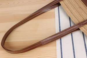 Detail of woven straw bag handle with dark brown leather and white contrast stitching