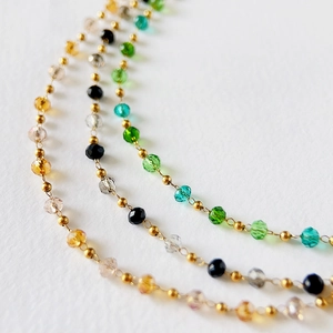 Macro shot of 2mm faceted crystal beads in green and amber on a 18k gold plated chain