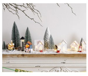 Close-up of glowing ceramic Christmas houses and miniature snowy trees on wood