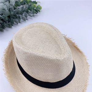 Close-up of beige woven straw hat with frayed edges and a black grosgrain ribbon band
