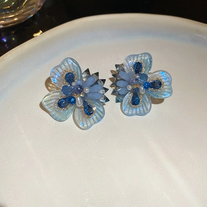 Macro detail of blue crystal flower earrings with pearls on a white ceramic tray