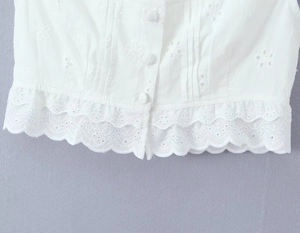 Détail du tissu blanc brodé avec ourlet festonné et fermeture à boutons sur le top