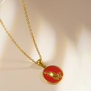 Vintage gold necklace with round red prayer hands pendant on beige fabric background