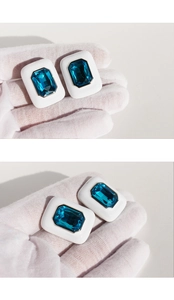 Macro detail of square blue zircon earrings with white enamel finish on hands